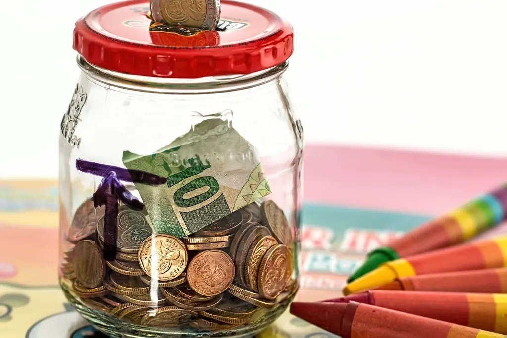 Glass jar filled with coins and a folded banknote, used as a simple savings jar