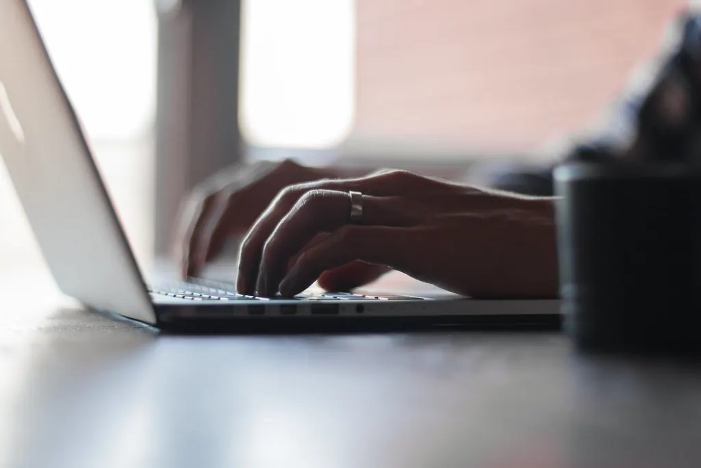 Close-up of hands typing on a laptop keyboard by a bright window