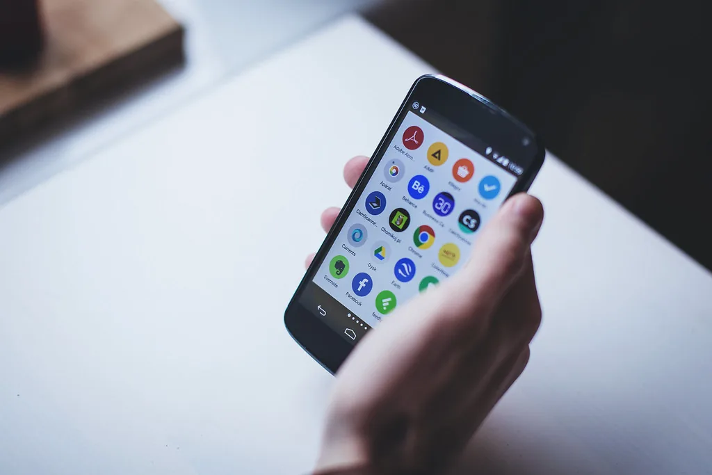 A hand holding a smartphone showing a grid of app icons