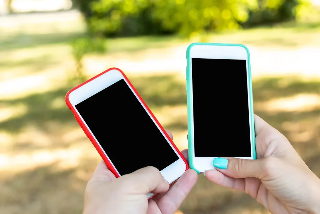 Two hands holding colourful smartphones outdoors