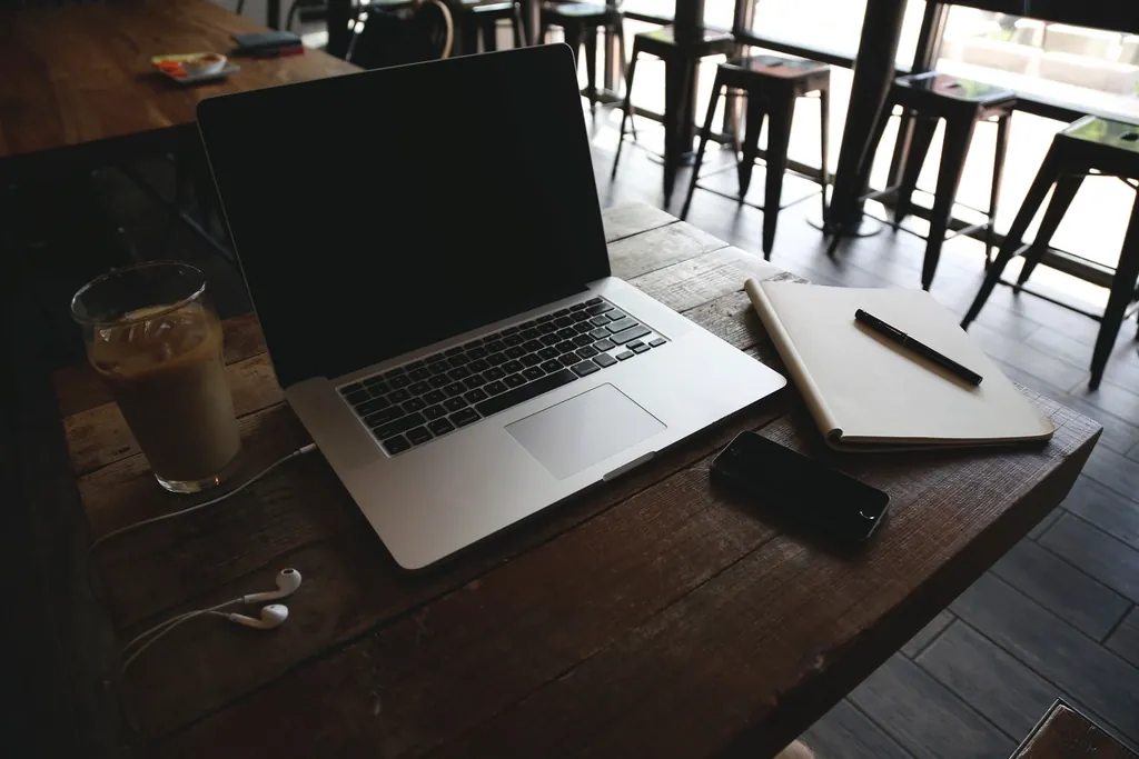 A laptop, iced coffee and notebook on a cafe table