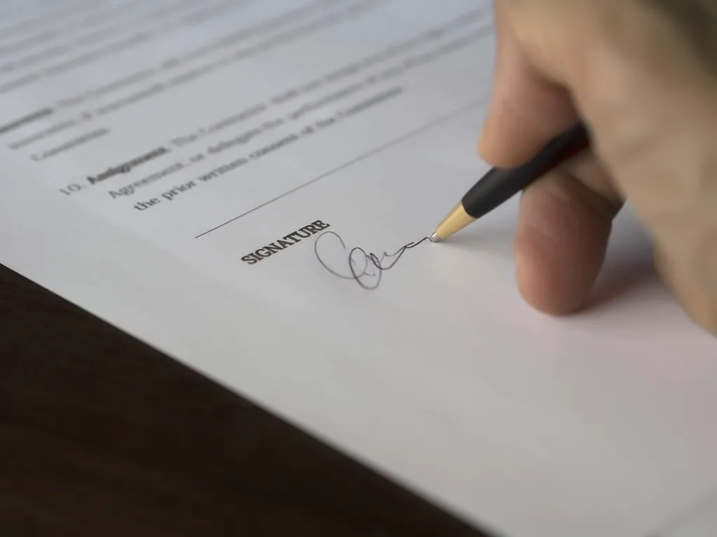 A hand signing a document on the signature line