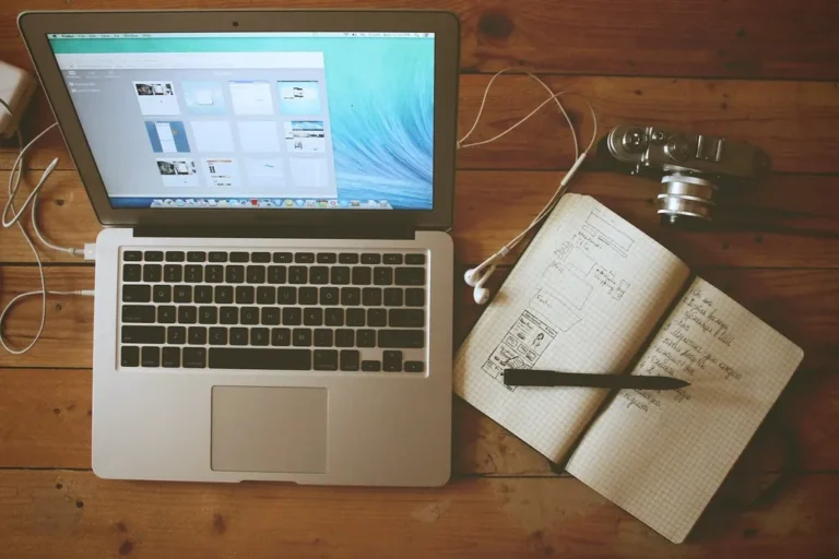 A laptop beside an open notebook with handwritten notes