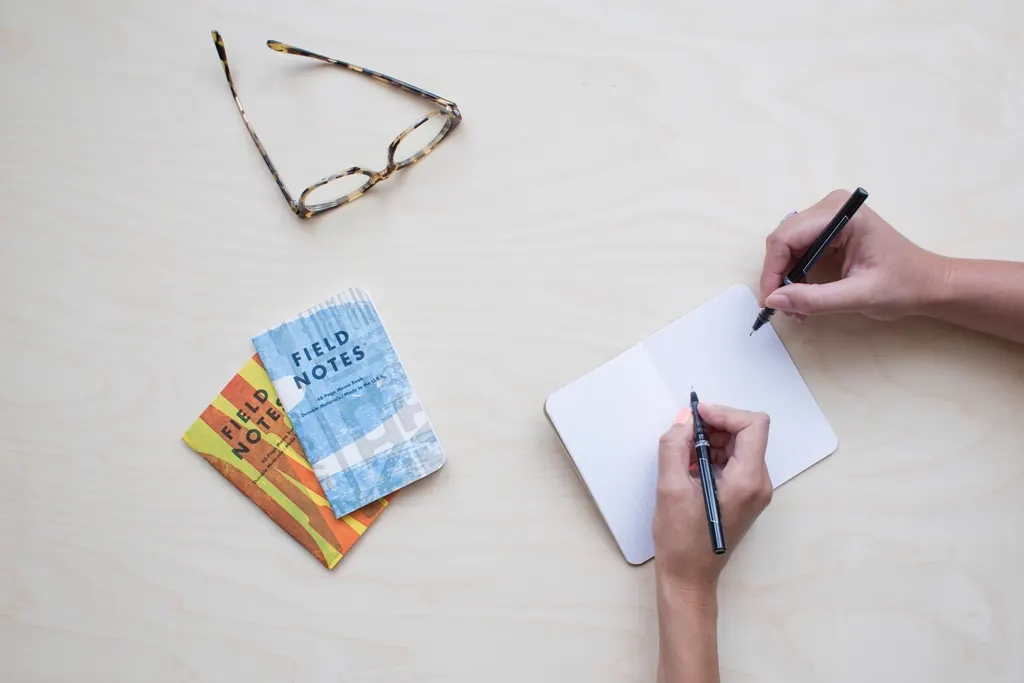 Person writing a quick note in a small pocket notebook with pen in hand